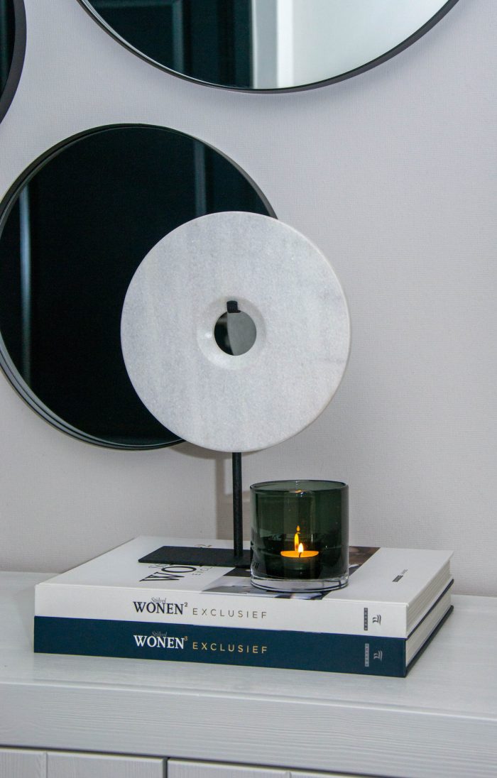 Bob Ornament Puck Wit – ronde marmeren schijf op zwarte standaard, gestyled op woonboeken met glazen windlicht