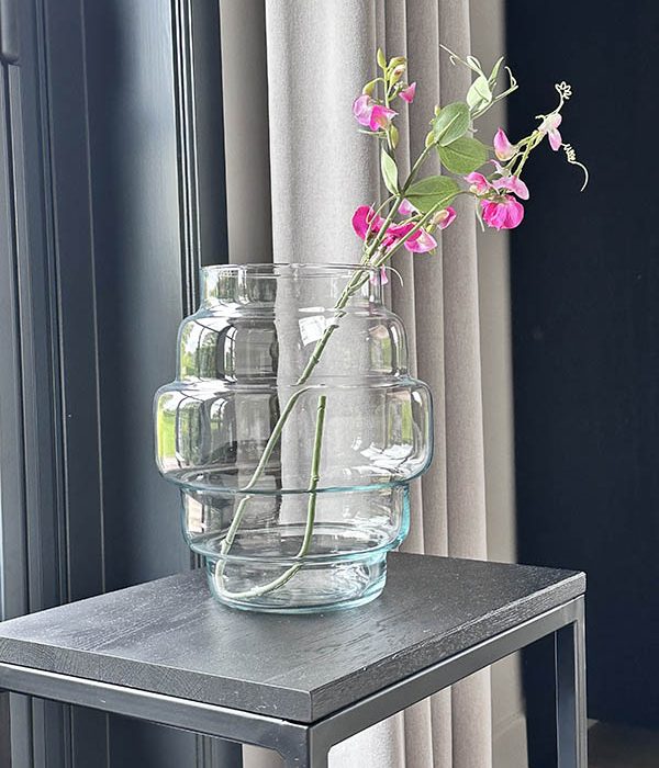 Glazen vaas Tess van Jodeco met transparante afwerking en organische vorm, gestyled met roze bloemen op een zwarte bijzettafel