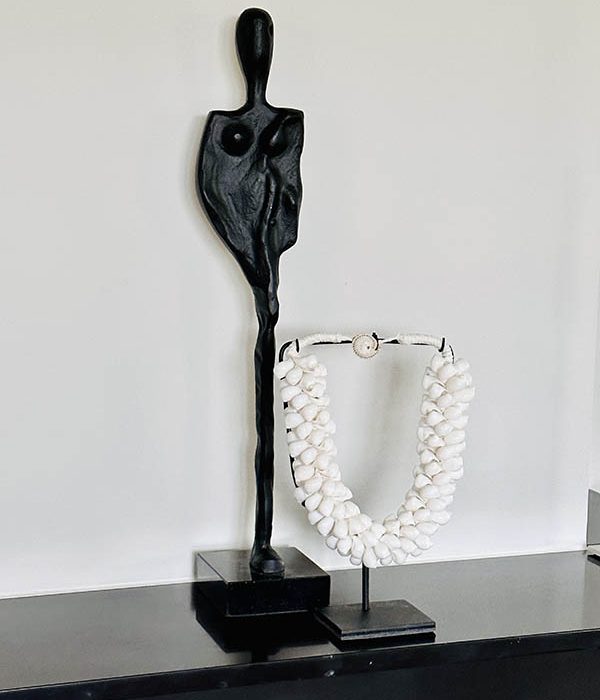 Witte schelpenketting Leen op standaard naast zwart abstract beeld op schouw"