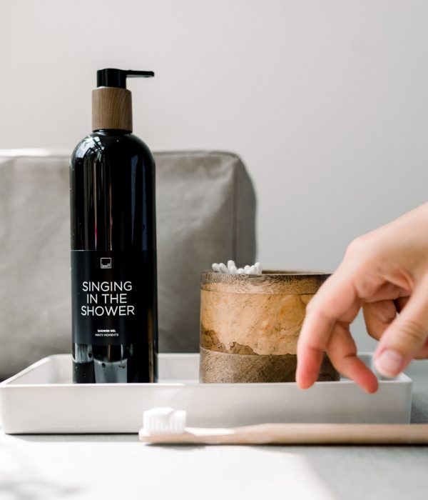 Leeff showergel ‘Singing in the Shower’ in zwarte pompflacon op een wit plateau, naast een houten bakje en een bamboe tandenborstel in een minimalistische badkamer setting.