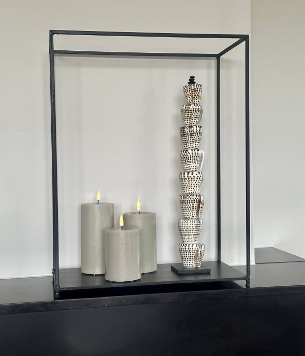 Deluxe Homeart LED stompkaarsen Sand in drie hoogtes (10, 12,5 en 15 cm) met real flame effect naast schelpenornament op zwarte schouw