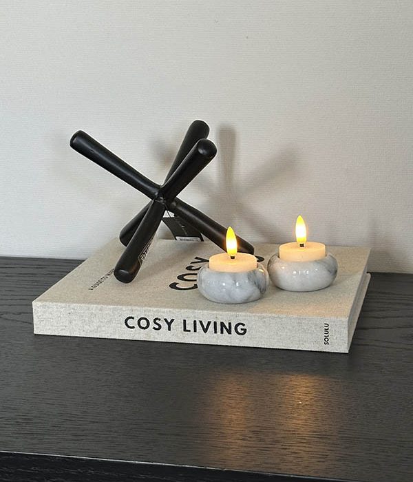 Set witte marmeren waxinelichthouders gestyled op een boek met een zwart woonaccessoire.