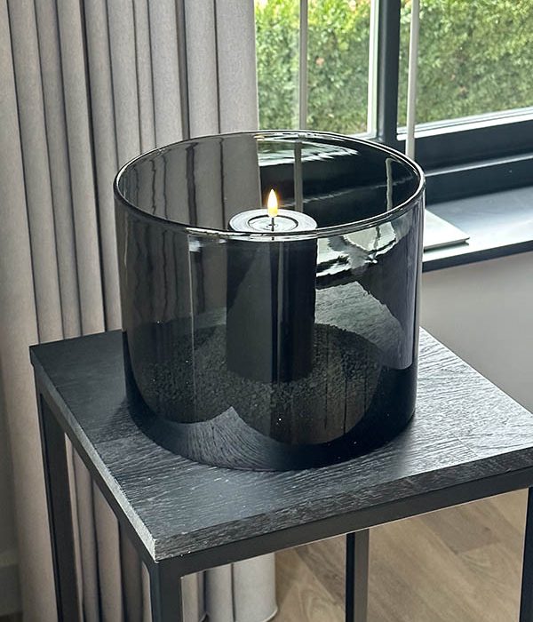 Deluxe Homeart LED stompkaars Sand met real flame effect, brandend in groot zwart windlicht op zwarte zuil